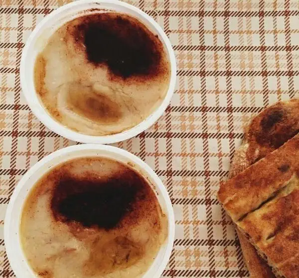 تصویری از دو کاسه حلیم خوش طعم و داغ از حلیم صبا با روغن حیوانی و دارچین، کنار نان سنگک تازه و سنتی برای صبحانه.