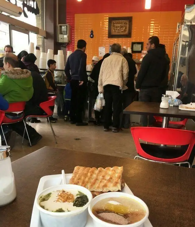 فضای پرجنب‌وجوش آش و حلیم پزی حلیم صبا، با مشتریان منتظر سفارش و میزی حاوی آش، حلیم و نان داغ آماده سرو.