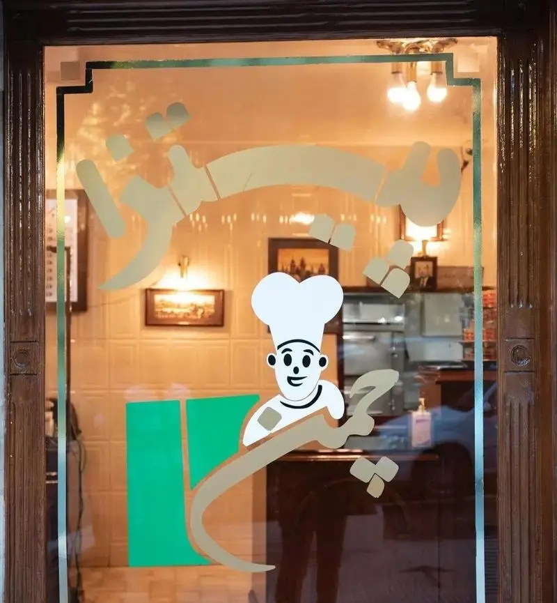 ورودی جذاب پیتزا چمن با برچسب لوگوی سرآشپز خندان و نام فارسی کسب و کار روی درب شیشه ای. بهترین فست فود و رستوران منطقه.