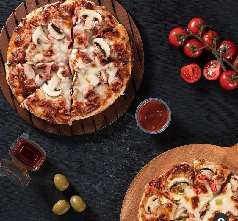 پیتزا چمن: دو پیتزای قارچ و سوسیس خوشمزه روی تخته چوبی، با زیتون، گوجه گیلاسی و سس. بهترین گزینه برای سفارش آنلاین پیتزا.