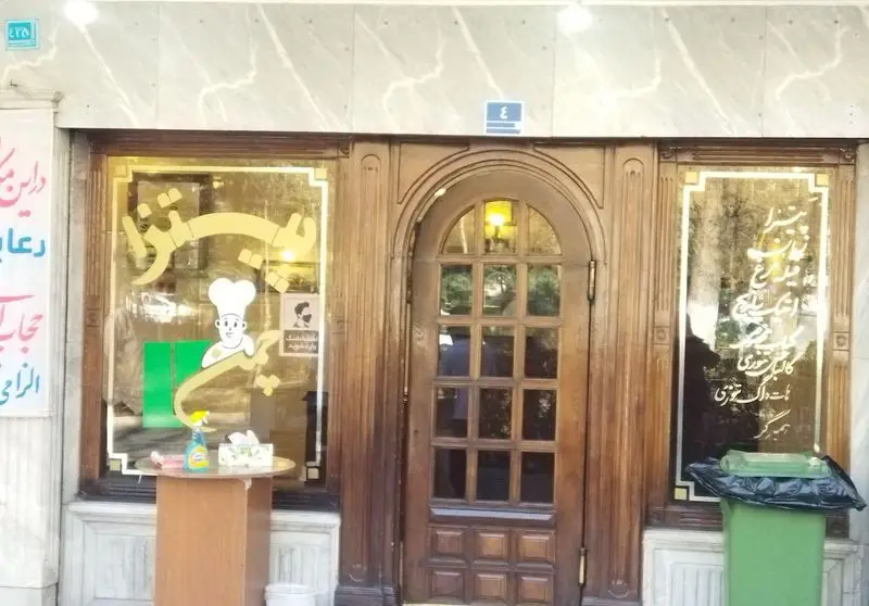 نمای بیرونی فست فود پیتزا چمن با درب ورودی چوبی شیک و پنجره‌های شیشه‌ای، آماده پذیرایی از مشتریان با کیفیت و طعم عالی.