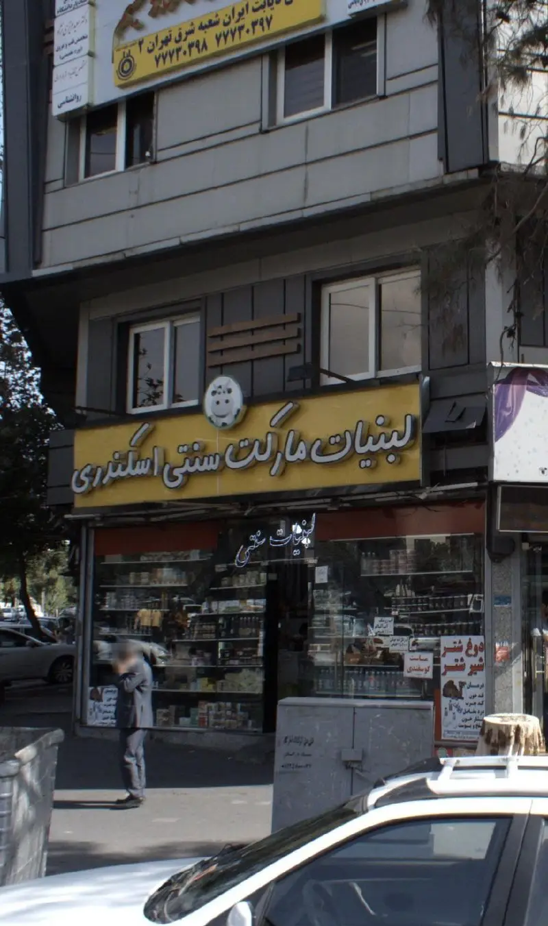 تصویر نمای بیرونی فروشگاه لبنیات مارکت سنتی اسکندری در تهران، با تابلوی زرد رنگ، ویترین پر از محصولات لبنی تازه و سنتی.
