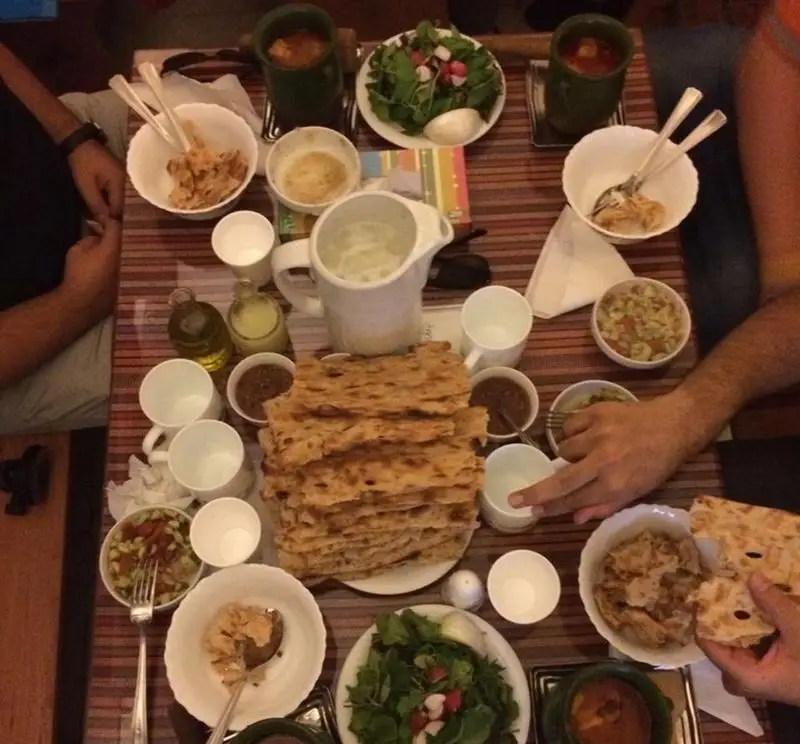 میز پر و پیمان رستوران دیزی با خوراک‌های سنتی ایرانی: دیزی، نان داغ، سالاد تازه و دوغ. تجربه‌ای اصیل از غذای خانگی.