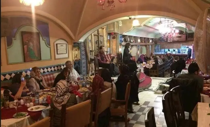 نمای داخلی رستوران دیزی با فضای سنتی و دلنشین، میزهای پر از مشتریان در حال شام، و اجرای موسیقی زنده برای لذت بیشتر میهمانان.