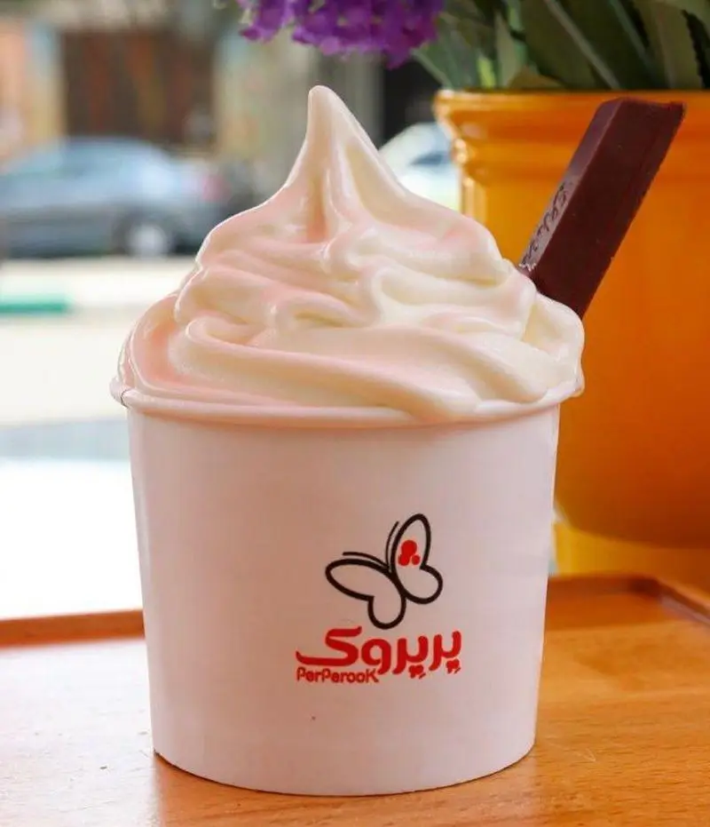 تصویری جذاب از بستنی سافت سرو سفید و خامه ای پرپروک، سرو شده در کاپ به همراه شکلات کیت کت، دسری دلپذیر از پیتزا پرپروک.