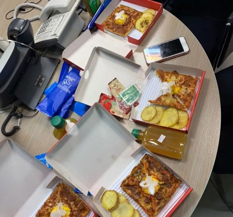 پیتزا پرپروک: جعبه‌های پیتزا مربعی با تخم مرغ و سیب‌زمینی کنار تلفن‌ها در محیط کار، آماده برای یک ناهار دلچسب یا دورهمی کاری.