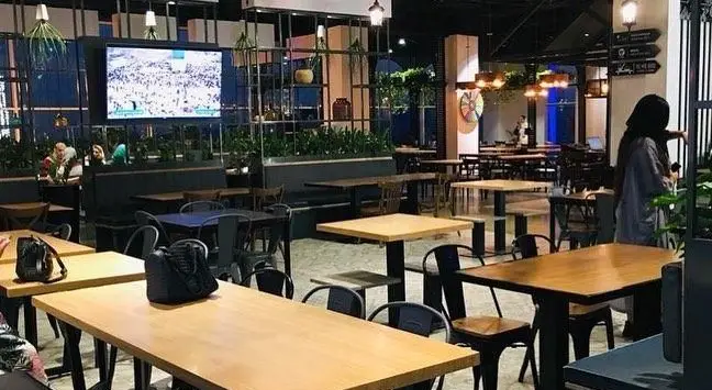 فضای داخلی مدرن و دلپذیر رستوران پیتزا پرپروک با میز و صندلی‌های چوبی و صفحه نمایش بزرگ، محیطی عالی برای تجربه غذا.