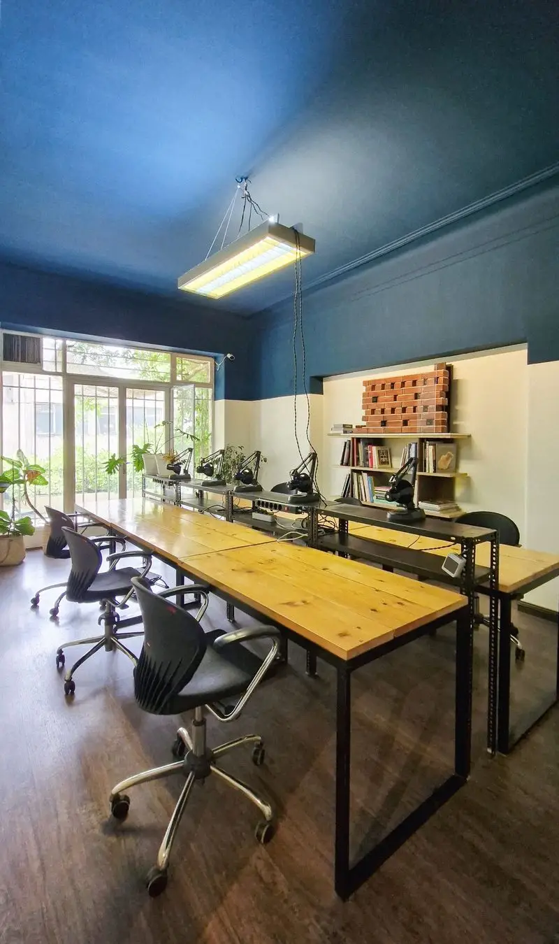 نمایی از فضای کار مشترک کافه کاربن با میزهای چوبی بزرگ، صندلی‌های اداری راحت، نور طبیعی فراوان و دکوراسیون داخلی منحصر به فرد.