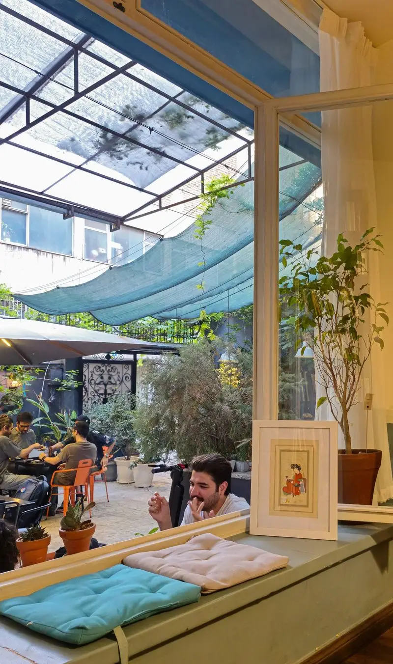 کافه و فضای کار کاربن: نمایی از محیط داخلی آرام و روشن با منظره فضای سبز بیرونی، مناسب برای کار، جلسات و استراحت زیر سایه‌بان.