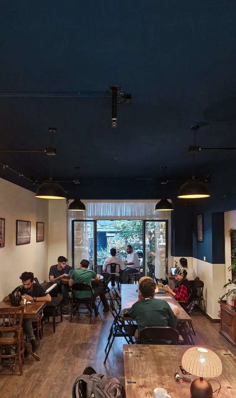 کافه و فضای کار مشترک کاربن با افراد مشغول کار و مطالعه، نورپردازی مدرن، میزهای چوبی و محیطی دلنشین برای تمرکز.