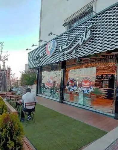 عکس نمای بیرونی فست فود برگر قلب سفید با تابلوی روشن، لوگوی قلب، فضای سبز، میز و صندلی برای مشتریان و دکوراسیون مدرن.