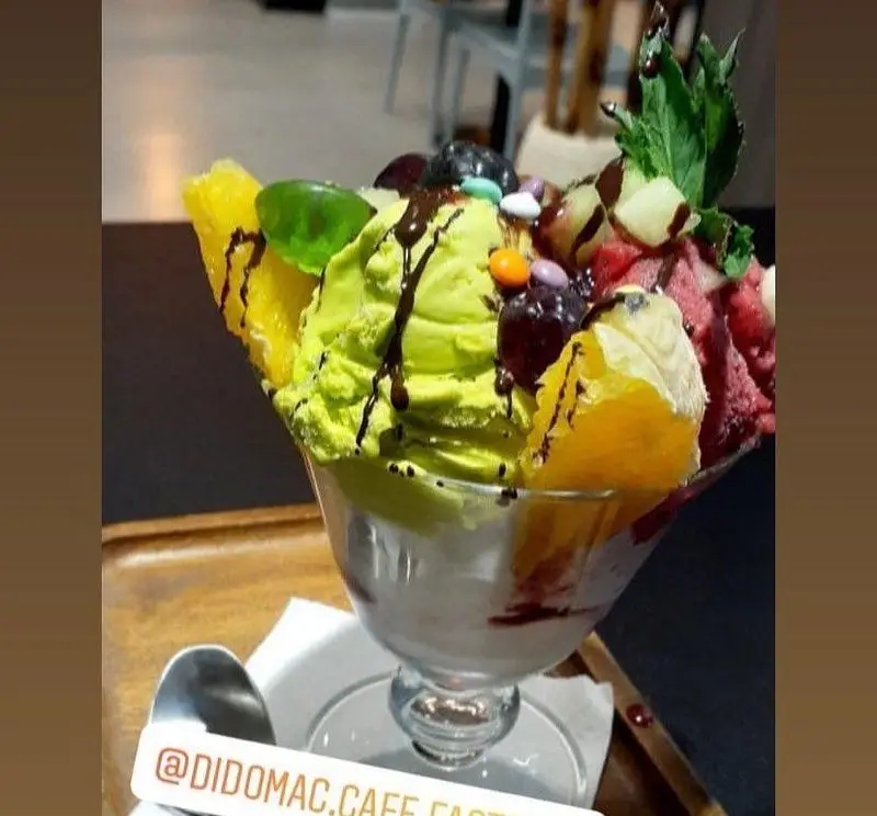 دسر بستنی میوه‌ای رنگارنگ کافه و فست فود دیدومک با اسکوپ‌های سبز، قرمز و سفید، تزئین شده با میوه تازه، شکلات و آبنبات.