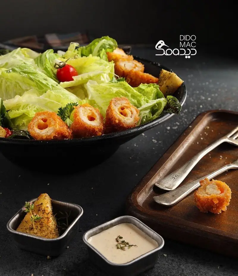 سالاد تازه با برگ‌های کاهو، گوجه گیلاسی و رول‌های مرغ سوخاری طلایی، به همراه سس و سیب‌زمینی از کافه و فست فود دیدومک