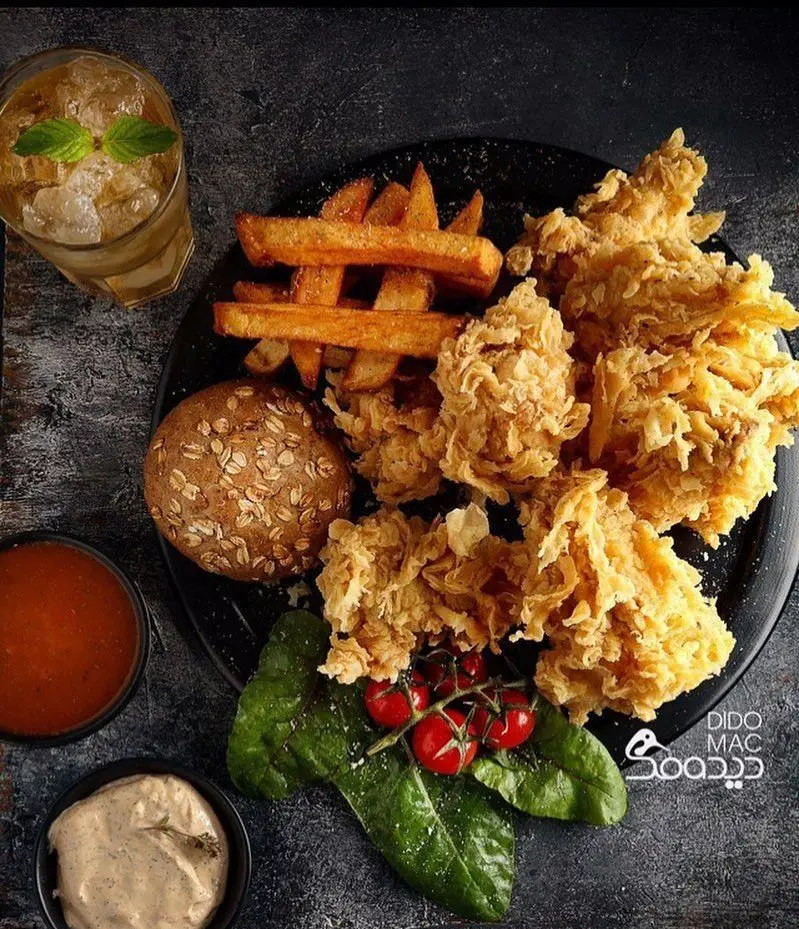 سفره‌ای اشتهاآور از کافه و فست فود دیدومک: مرغ سوخاری ترد، سیب‌زمینی سرخ‌کرده، نان سبوس‌دار، نوشیدنی خنک و سس، با تزئین گوجه و سبزی.