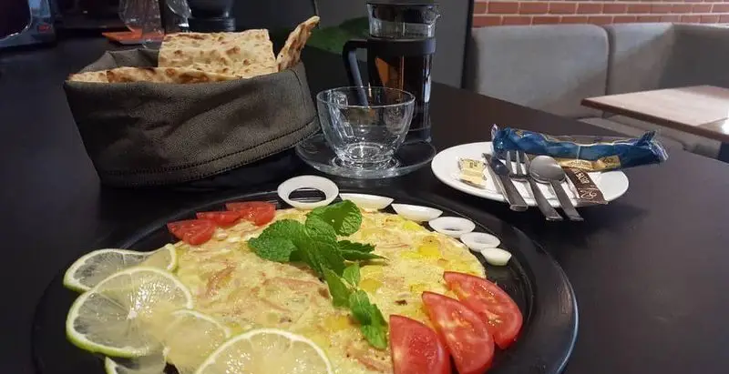 صبحانه کامل کافه و فست فود دیدومک شامل املت، نان تازه، برش‌های لیمو، گوجه، نعناع، پیاز، چای و قاشق و چنگال