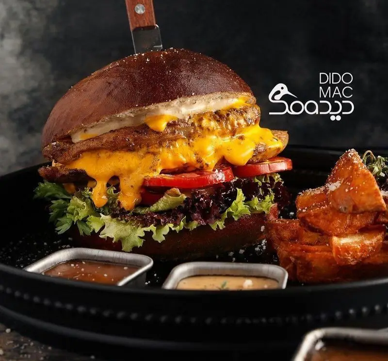 تصویری جذاب از همبرگر دیدومک با پنیر چدار آب شده، کاهو، گوجه و پتی‌های آبدار، همراه با سیب‌زمینی رستیک و سس‌های متنوع در کافه فست فود دیدومک.