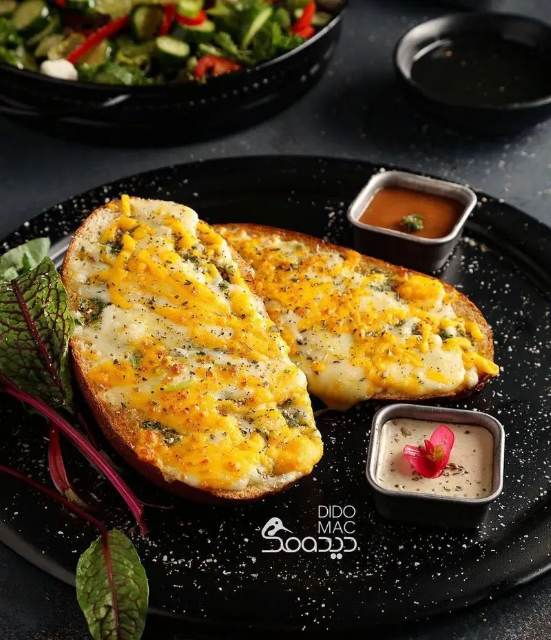 نان سیر و پنیر طلایی با چاشنی‌های خوشبو و سس‌های متنوع از منوی کافه و فست فود دیدومک، همراه با سالاد.