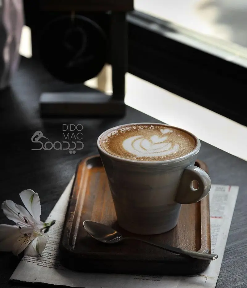 قهوه لاته آرت دلپذیر با طرح قلب در کافه دیدومک، روی میز کافه با سینی چوبی. لذت تجربه نوشیدنی‌های گرم و فست‌فود در دیدومک.