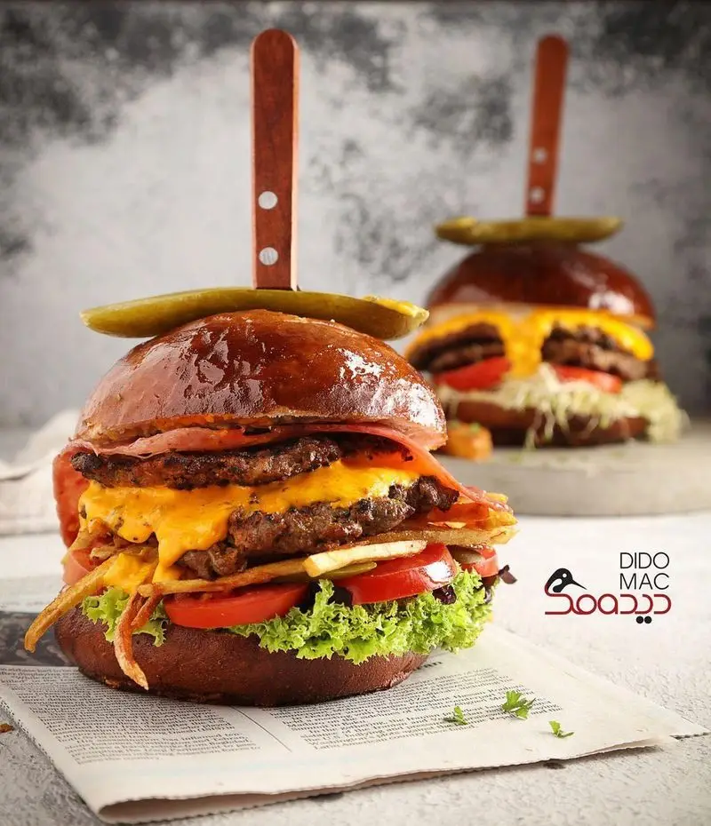 تصویر دو برگر لذیذ دیدومک با دو پتی گوشت، پنیر آب شده، بیکن، کاهو و سیب زمینی سرخ شده روی نان برگر.