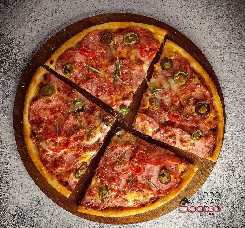 پیتزای لذیذ و داغ دیدومک با سوسیس، فلفل سبز تند، قرمز و رزماری روی تخته چوبی. انتخابی عالی از کافه و فست فود دیدومک.