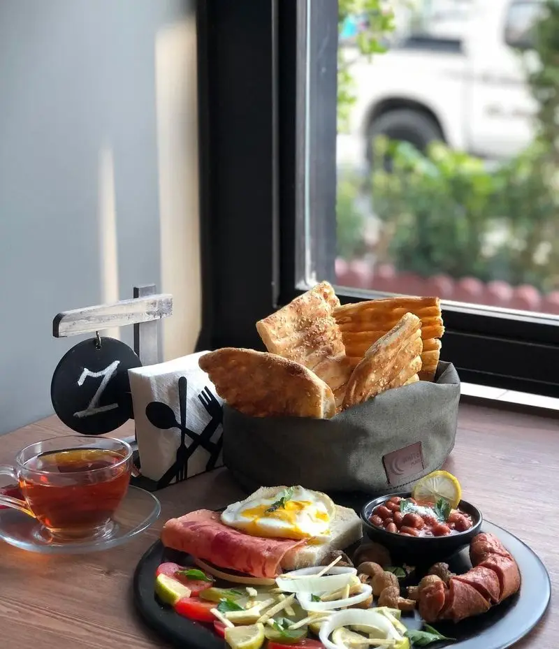 صبحانه ایرانی و فرنگی متنوع کافه و فست فود دیدومک: نان تازه، تخم مرغ، سوسیس، لوبیا، سالاد و چای کنار پنجره.