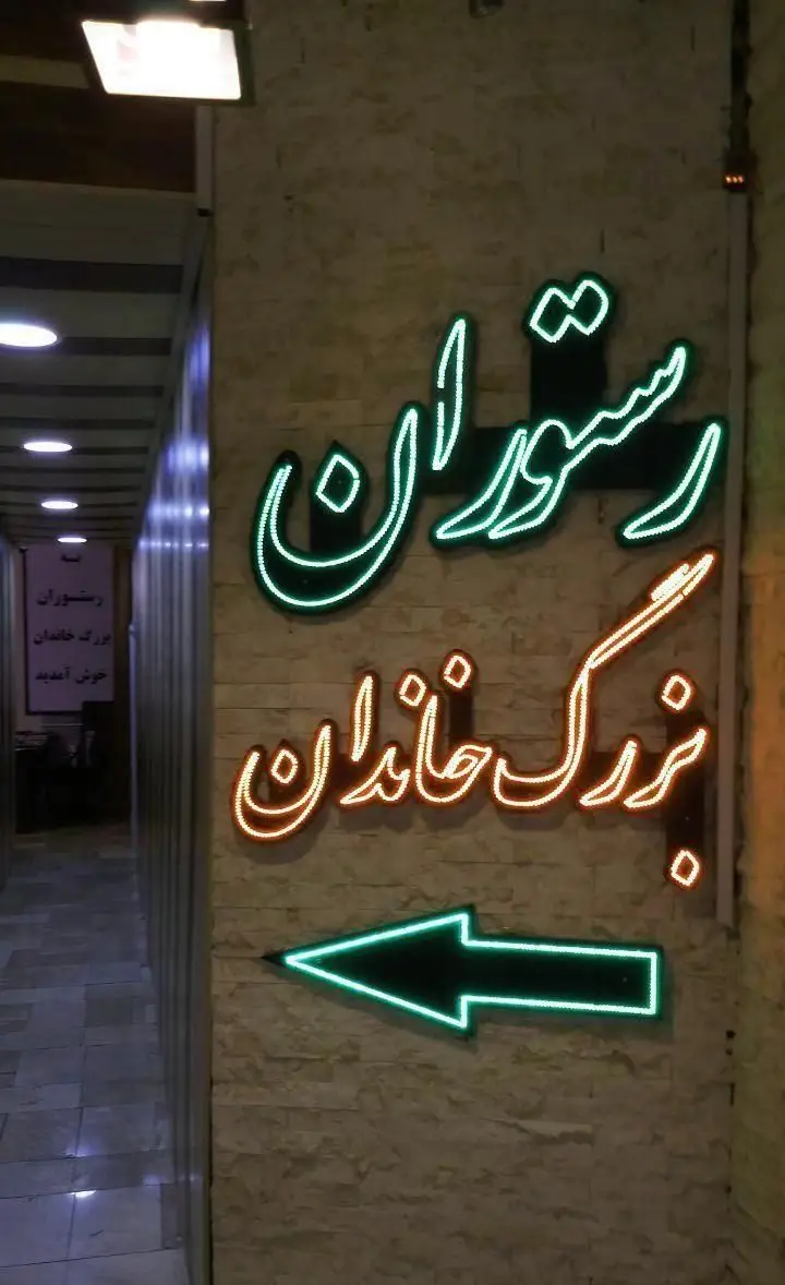 تابلو نئون درخشان رستوران ایرانی بزرگ خاندان، شامل نام رستوران و فلش سبز رنگ جهت‌نما برای راهنمایی مشتریان به ورودی.