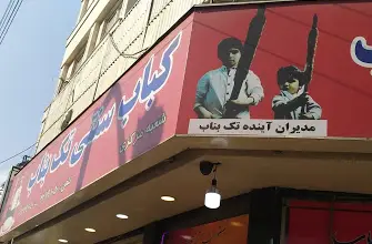 نمای بیرونی رستوران کبابسرای تک بناب، تابلوی بزرگ حاوی نام و لوگو، به همراه تصویر تبلیغاتی جذاب کودکان با سیخ کباب.