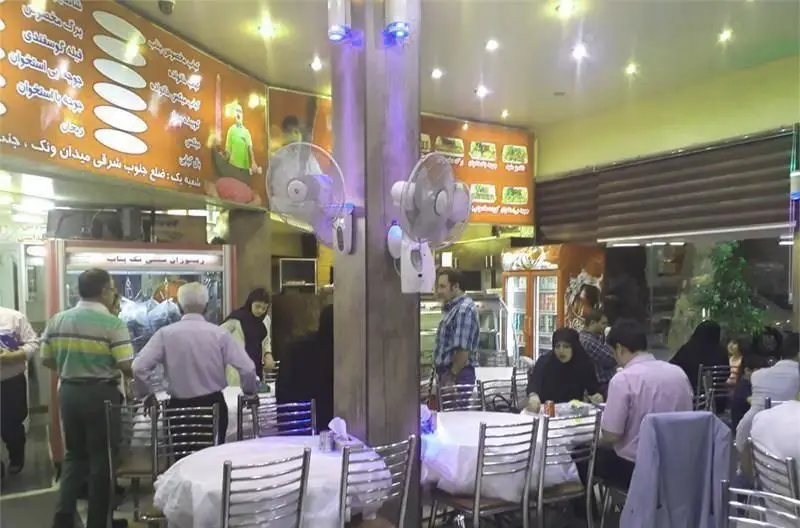 فضای داخلی دلنشین و پرنور کبابسرای تک بناب، با حضور مشتریان در حال صرف کباب و دیگر غذاها در محیطی گرم و شلوغ.