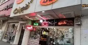 نمای بیرونی کافه فنجون، با تابلوی نئون روشن فنجان قهوه، در خیابان شلوغ شهر. این کافه محیطی دلنشین برای صرف قهوه و نوشیدنی‌ها فراهم کرده است.