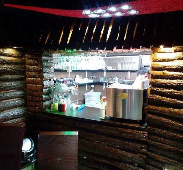 فضای داخلی دنج و دلنشین کافه رستوران گلایل؛ نمای قسمت بار با دیوارهای روستیک چوبی، سقف قرمز و نورپردازی جذاب، پرسنل در حال آماده‌سازی.