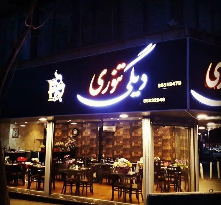 نمای خارجی روشن رستوران دیگی تنوری در شب با تابلو نئون، لوگوی منحصر به فرد و دکوراسیون داخلی گرم و صمیمی با میز و صندلی.