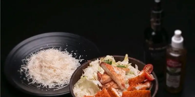 سالاد سزار مرغ سوخاری تازه و خوشمزه فست فود دی نایت با پنیر پارمزان رنده شده، انتخابی عالی برای یک وعده سالم و لذیذ در رستوران.
