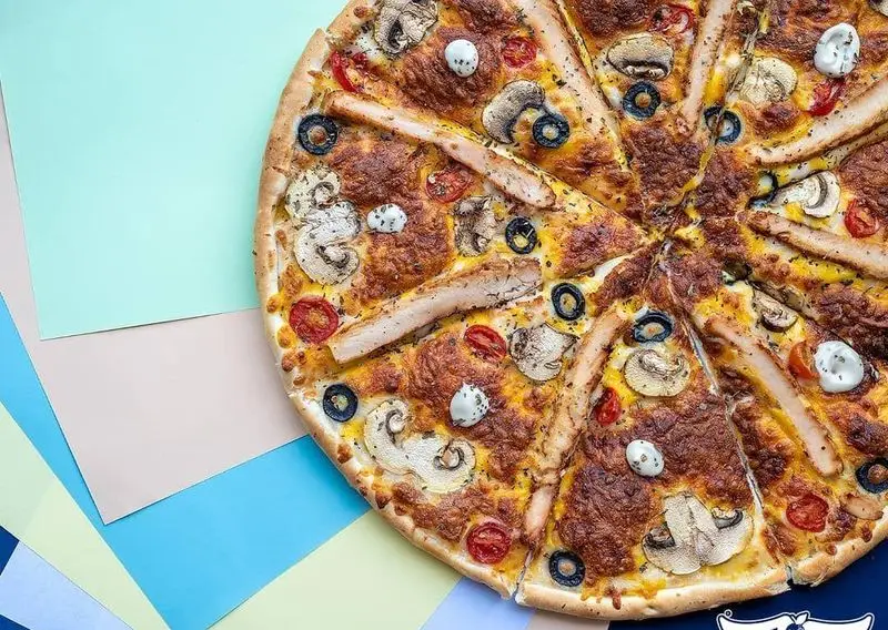 تصویری جذاب از پیتزا بزرگ و خوشمزه پیتزا سیب با تکه‌های مرغ گریل، قارچ تازه، زیتون سیاه و گوجه گیلاسی. مناسب سفارش آنلاین.