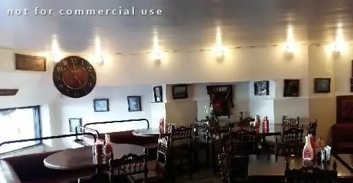 نمای داخلی رستوران فست فود پیتزا پیشخوان با چیدمان میز و صندلی‌های چوبی، نیمکت‌های راحت، ساعت دیواری بزرگ و نورپردازی مناسب محیط.