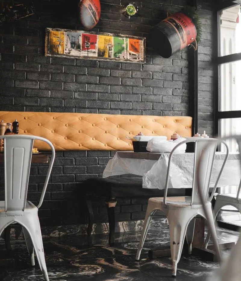نمای داخلی شیک و مدرن فست فود پلاس با دیوار آجری، نیمکت راحتی، میز و صندلی‌های فلزی با طراحی صنعتی جذاب.