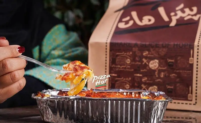 لذت بردن از غذای گرم و خوشمزه پیتزا هات اکباتان. یک وعده غذایی لذیذ در ظرف بیرون‌بر آلومینیومی با پنیر طلایی و ذوب‌شده، آماده برای سرو.