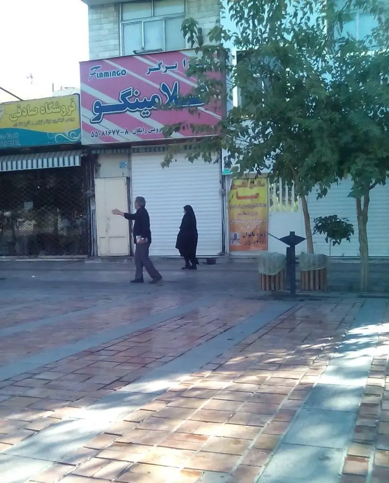 نمای خیابانی از رستوران پیتزا برگر فلامینگو با تابلو صورتی بزرگ حاوی نام و شماره تماس. عابران در پیاده‌روی شهر ایران.