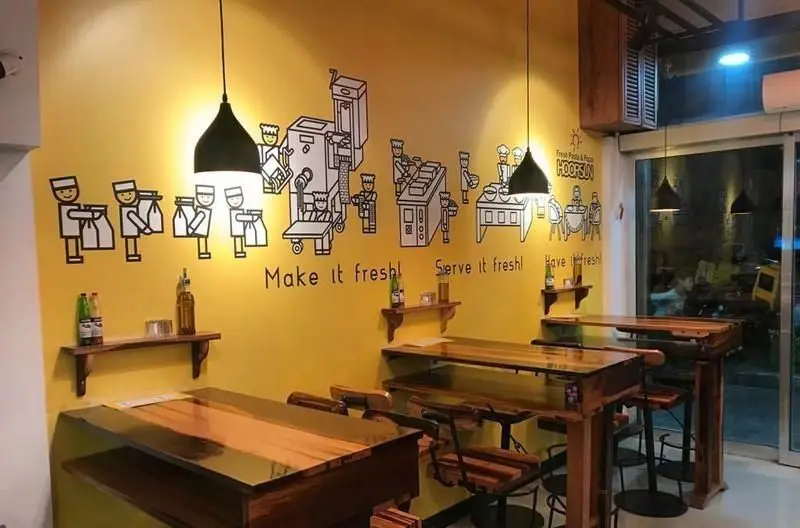 دکوراسیون داخلی رستوران ایتالیایی هورسان با دیوار زرد، نقاشی‌های فرایند تهیه غذای تازه، میزهای چوبی و فضای دلنشین برای پاستا و پیتزا.