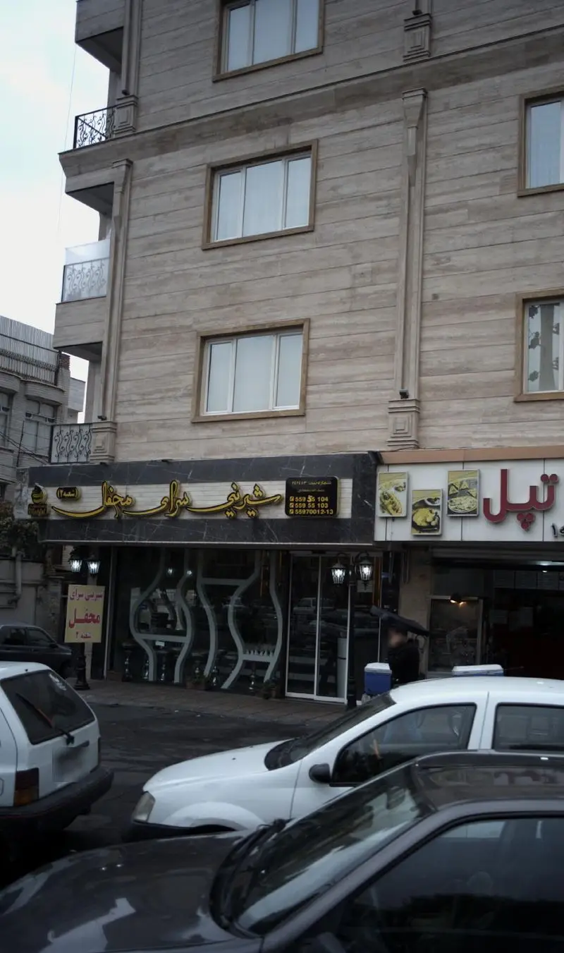 عکس از شیرینی سرای محفل در تهران، یک قنادی مدرن با نمای سنگی و پنجره‌های متعدد. نمای خیابان با اتومبیل‌ها.