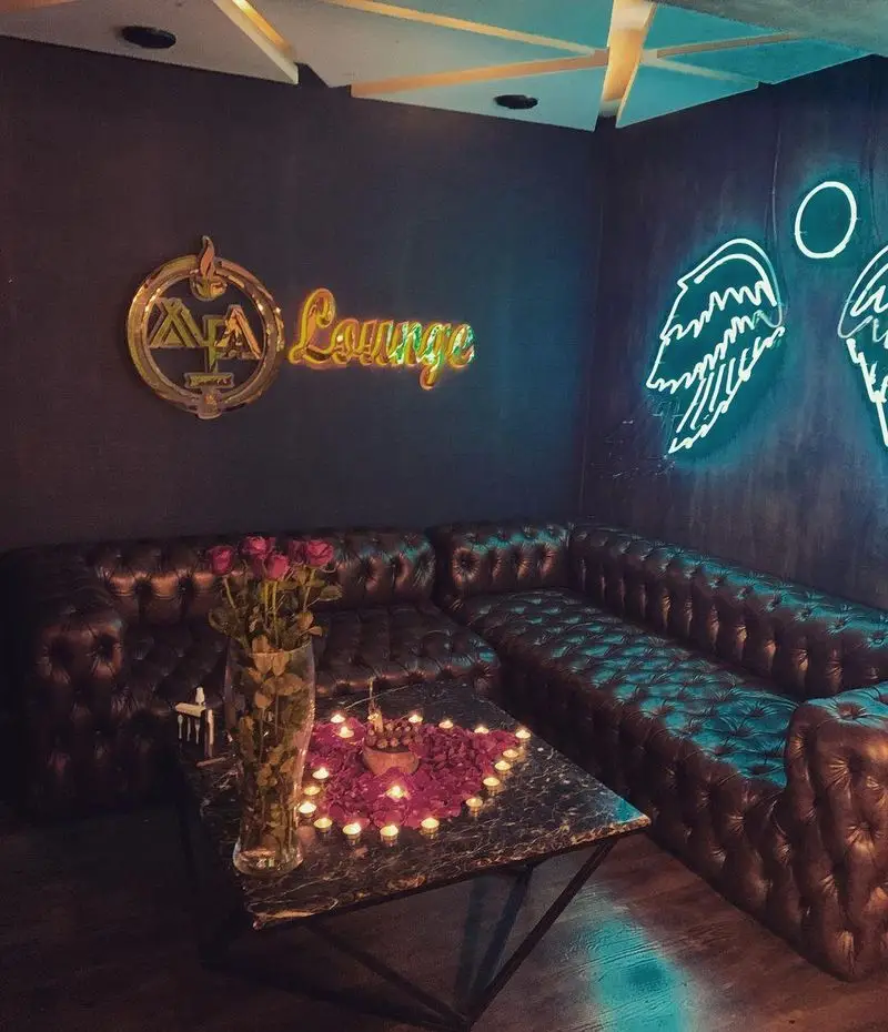 فضای داخلی دنج کافه رستوران آلپا با مبلمان چرمی شیک، نورپردازی نئون "Alpa Lounge" و میز تزئین شده رمانتیک با شمع و گل رز.