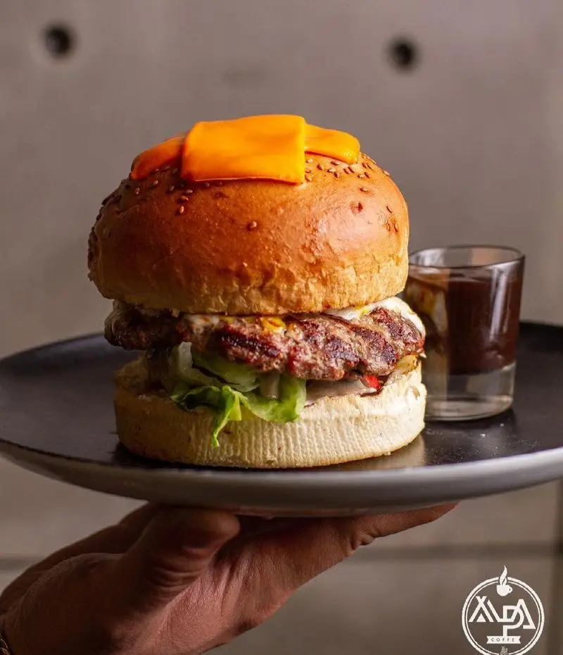 همبرگر ویژه کافه رستوران آلپا با نان تازه، گوشت مرغوب، پنیر ورقه‌ای و کاهو، همراه با سس مخصوص در بشقاب. انتخابی لذیذ برای شما.