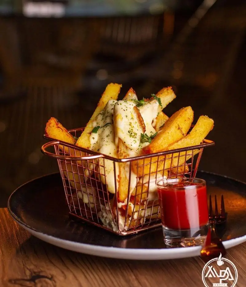 سیب زمینی سرخ کرده با سس پنیر و سبزیجات معطر در کافه رستوران آلپا، همراه با کچاپ، یک غذای خوشمزه و محبوب.