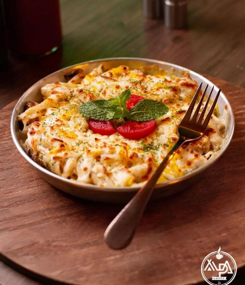 پاستا پنیری خوشمزه و طلایی، تزئین شده با نعناع و گوجه فرنگی، آماده سرو در سینی چوبی، از منوی کافه رستوران آلپا.