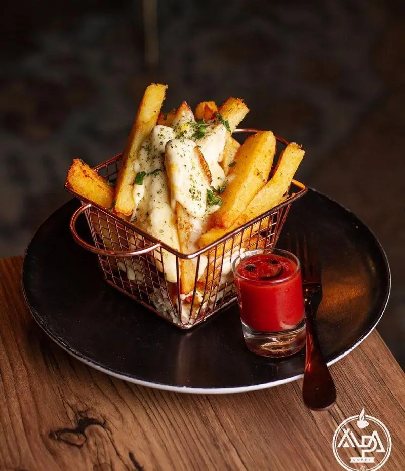 تصویری جذاب از سیب‌زمینی سرخ‌کرده پنیری ویژه و خوشمزه با سس کچاپ خندان، در فضای دلنشین کافه رستوران آلپا.