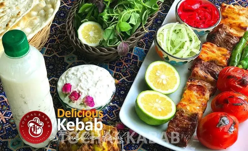 نمای اشتهاآور از انواع کباب‌های لذیذ توچال کباب همراه با نان تازه، دوغ، سبزی، ماست و مخلفات در سفره سنتی ایرانی.