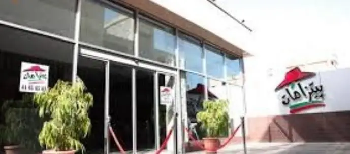 نمای بیرونی رستوران فست فود پیتزا آمات با ورودی شیشه‌ای، تابلوی بزرگ حاوی لوگوی کلاه و نام و شماره تلفن