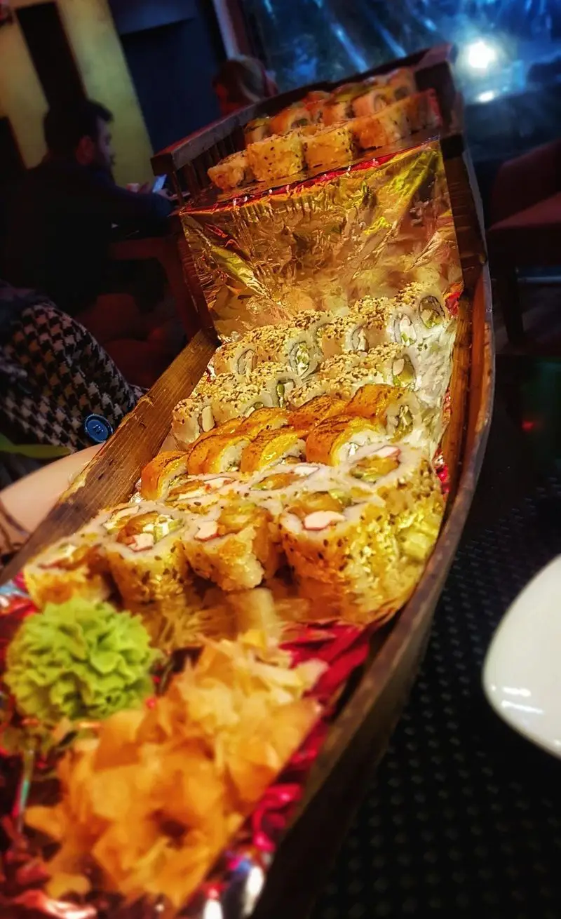 نمای نزدیک از یک قایق سوشی بزرگ و پر از رول‌های متنوع سوشی خونه. شامل واسابی و زنجبیل، انتخابی عالی برای دوستداران غذای ژاپنی.