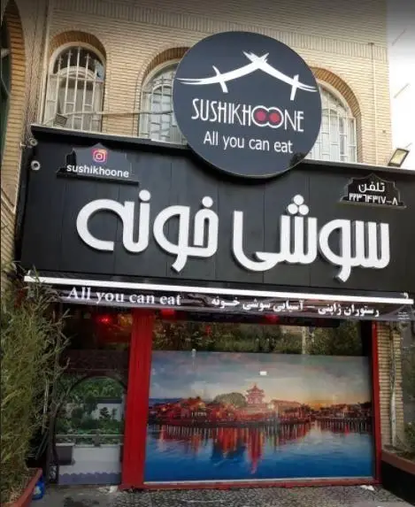 نمای بیرونی رستوران سوشی خونه، تابلوی مشکی بزرگ با نام SUSHIKHOONE و عبارت «All you can eat». یک رستوران سوشی عالی با منوی آزاد.