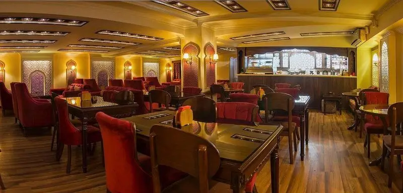 رستوران سوشی خونه با دکوراسیون گرم و مجلل، میزهای چوبی و صندلی‌های راحت قرمز، فضایی دعوت‌کننده برای صرف سوشی و غذاهای خاص.