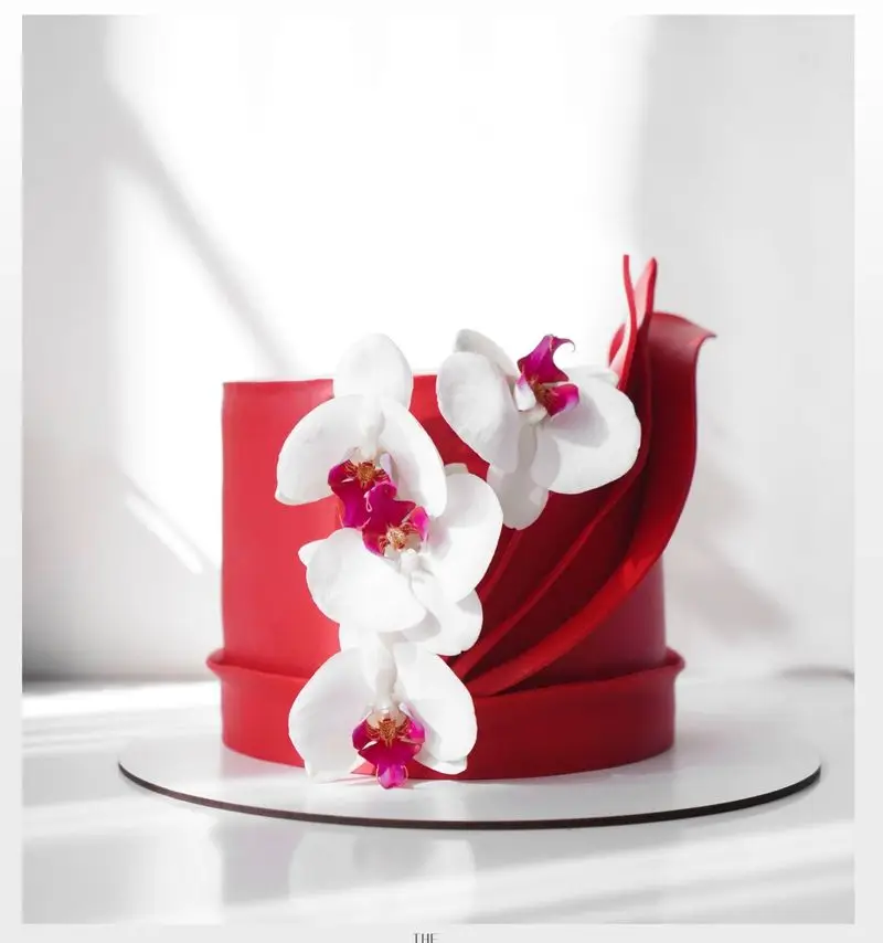 کیک تولد قرمز لوکس و خاص از میس کیک با ارکیده‌های سفید زیبا و طراحی مدرن، مناسب برای سفارش کیک‌های سفارشی و لاکچری شما.